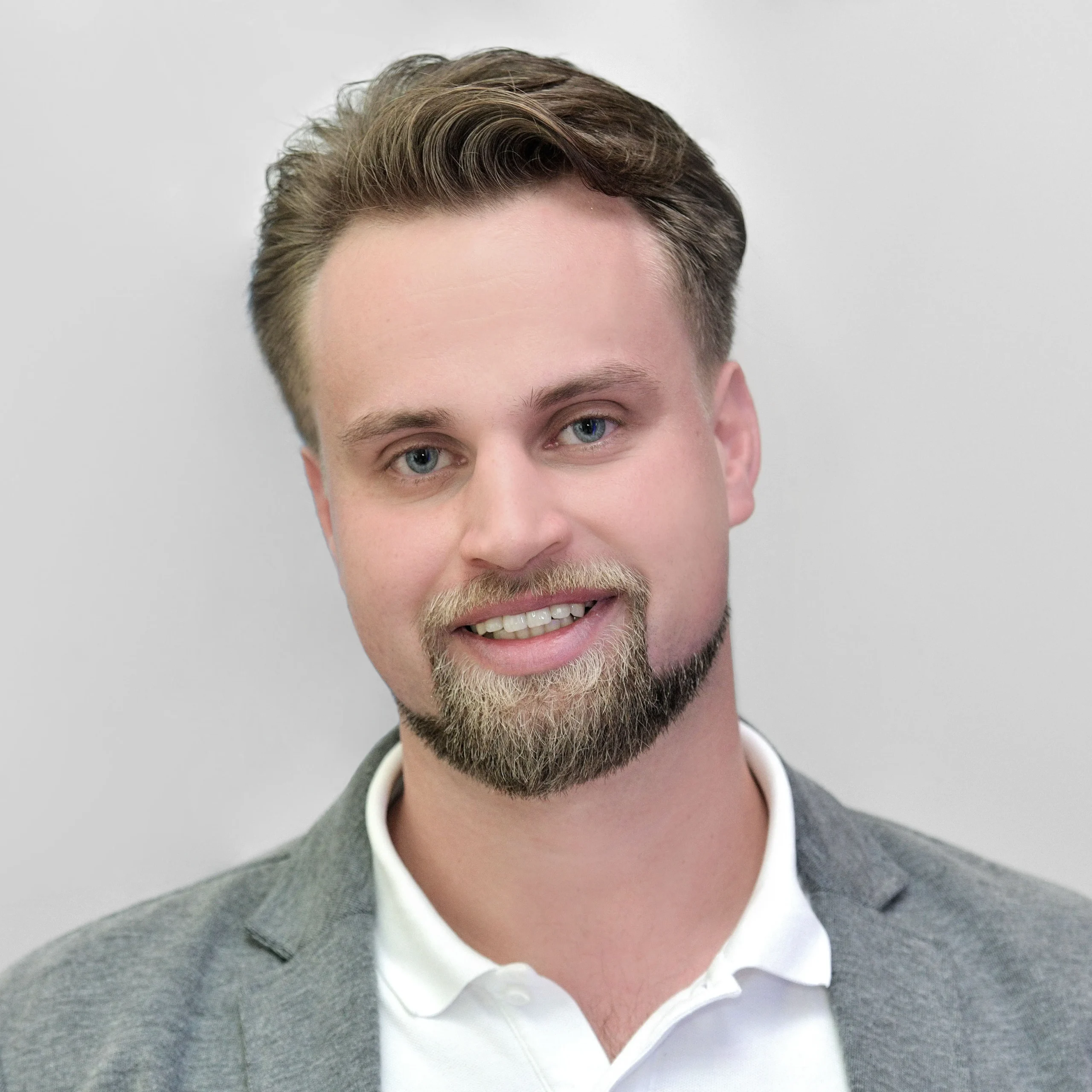 Porträt von Philipp Unger mit Bart und Sakko vor hellem Hintergrund.